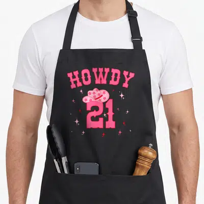 Groovy cowgirl aprons - Pink HOWDY 21 text with star-patterned cowboy hat and sparkles — shown on a black cotton canvas apron against a white background