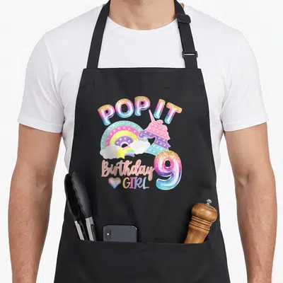 Pop birthday apron - Unicorn pop it toy, rainbow, and number 9 birthday girl text — shown on a black cotton canvas apron against a white background
