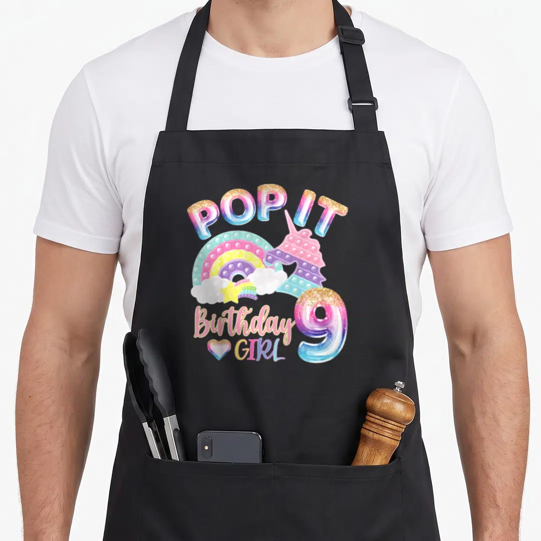 Pop birthday apron - Unicorn pop it toy, rainbow, and number 9 birthday girl text — shown on a black cotton canvas apron against a white background