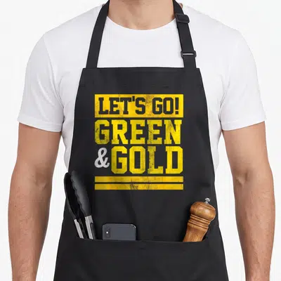 Retro game aprons - Yellow and white block letters reading LET'S GO GREEN AND GOLD with two bottom bars — shown on a black cotton canvas apron against a white background
