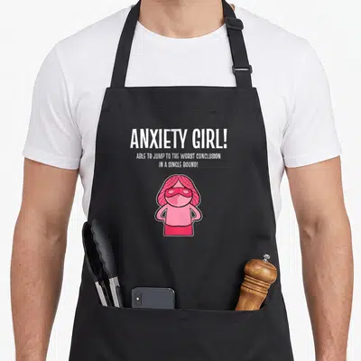 Cute anxiety anxious apron - Pink cartoon girl wearing a mask under white text ANXIETY GIRL! ABLE TO JUMP TO THE WORST — shown on a black cotton canvas apron against a white background
