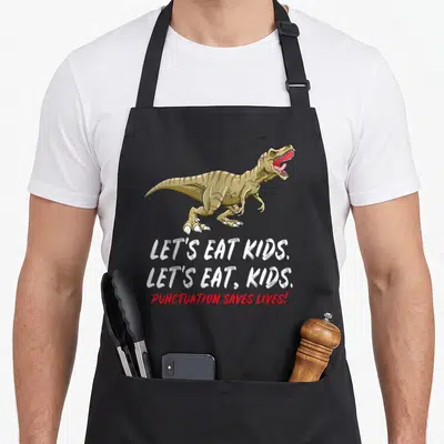 School let's eat apron - Brown T-Rex above white and red text reading Let's Eat Kids Punctuation Saves Lives — shown on a black cotton canvas apron against a white background