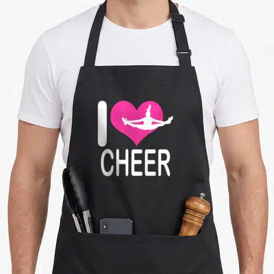 Cute cheer cheerleading apron - Pink heart with white cheerleader silhouette and I CHEER text — shown on a black cotton canvas apron against a white background