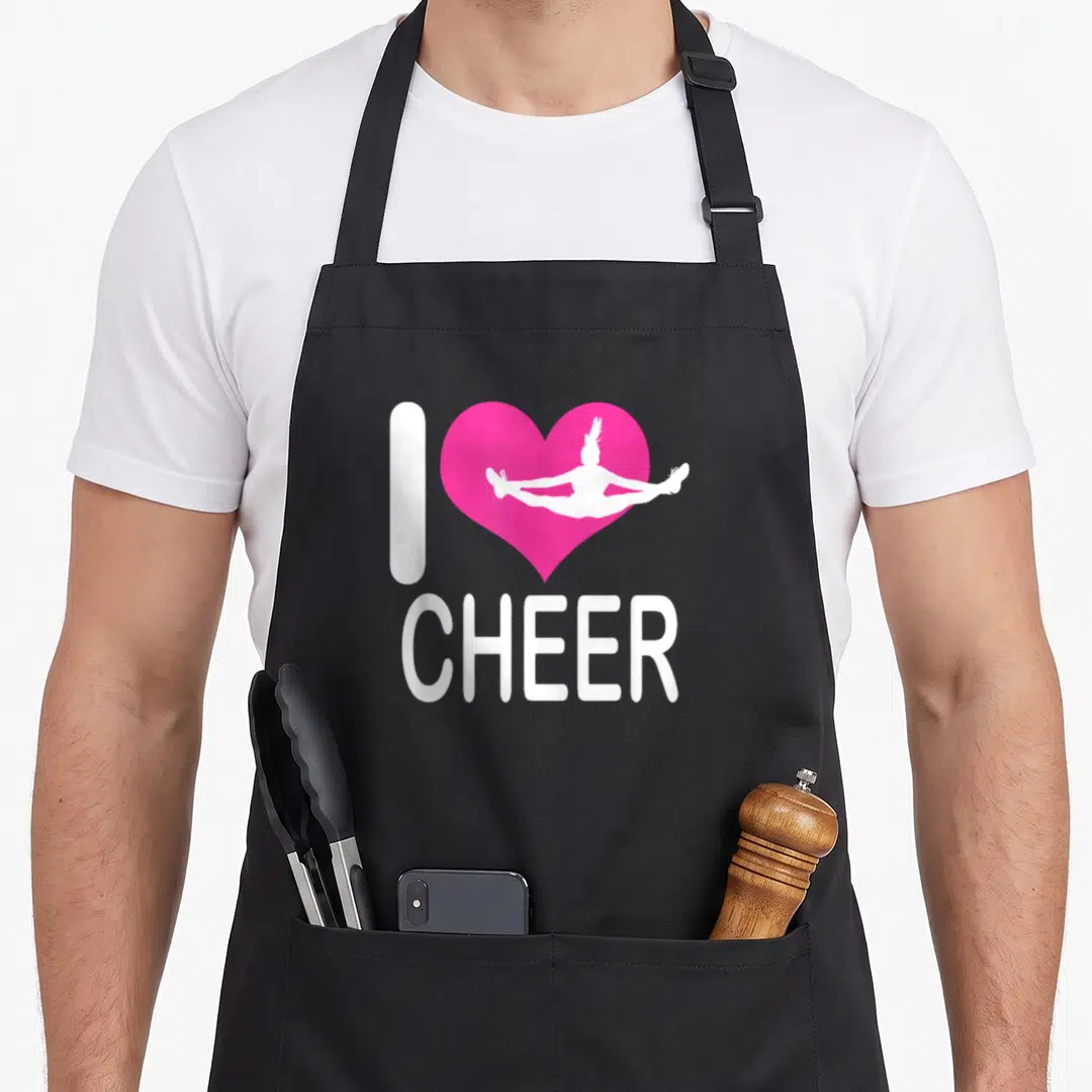 Cute cheer cheerleading apron - Pink heart with white cheerleader silhouette and I CHEER text — shown on a black cotton canvas apron against a white background