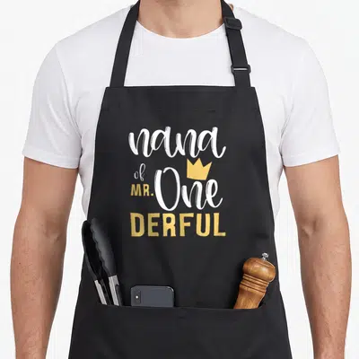 Onederful nana aprons - Stacked white and yellow text reading nana of MR One DERFUL with a small crown icon above — shown on a black cotton canvas apron against a white background
