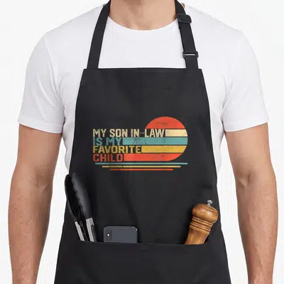 Cute funny son in law apron - Retro sun and stripes with stacked text MY SON IN-LAW IS MY FAVORITE CHILD — shown on a black cotton canvas apron against a white background