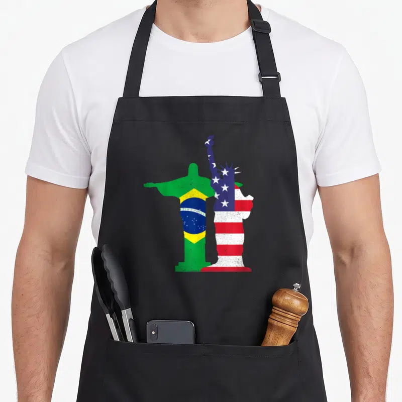 Culture american flag apron - Two statue silhouettes filled with Brazilian and USA flag colors and Ordem e Progresso — shown on a black cotton canvas apron against a white background