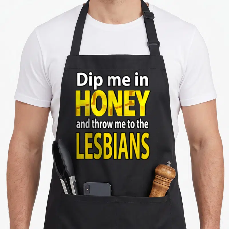 Dip throw apron - Stacked yellow and white text reading Dip me in HONEY and throw me to the LESBIANS with black outlines — shown on a black cotton canvas apron against a white background