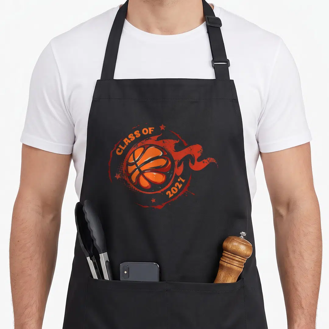 Basketball student aprons - Orange cartoon basketball surrounded by flames and stars with Class of 2021 text — shown on a black cotton canvas apron against a white background