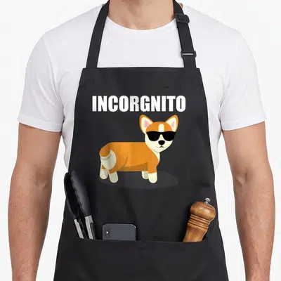 Incorgnito corgi apron - Cartoon corgi in black sunglasses below white INCORGNITO text — shown on a black cotton canvas apron against a white background