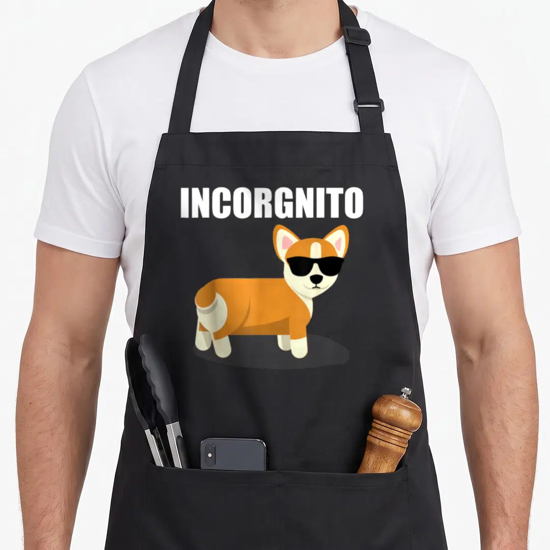 Incorgnito corgi apron - Cartoon corgi in black sunglasses below white INCORGNITO text — shown on a black cotton canvas apron against a white background