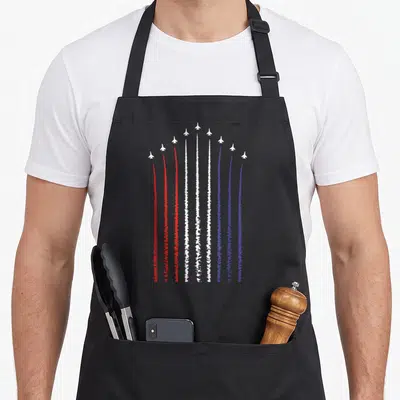 Flag fighter 4th of july apron - Eleven white jets flying in V-formation with red white and blue smoke trails — shown on a black cotton canvas apron against a white background