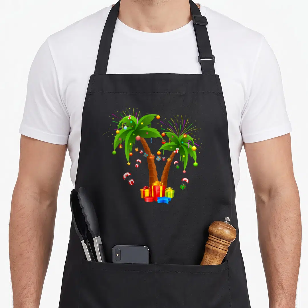 Tropical christmas tree apron - Two decorated palm trees with presents, parachutes, and fireworks in green red yellow — shown on a black cotton canvas apron against a white background