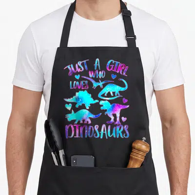 Watercolor dinosaur apron - Four dinosaurs and hearts in blue pink purple watercolor style with text — shown on a black cotton canvas apron against a white background