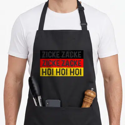 Zicke german apron - ZICKE ZACKE HOI HOI text on black red yellow distressed stripes — shown on a black cotton canvas apron against a white background