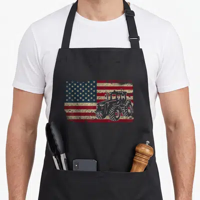 Tractor farm apron - White tractor outline over distressed red white blue American flag — shown on a black cotton canvas apron against a white background