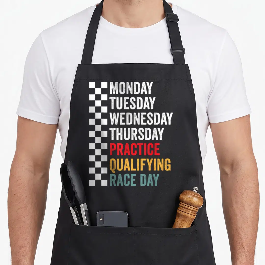 Monday practice apron - Stacked text listing days and race phases beside a checkered flag strip — shown on a black cotton canvas apron against a white background