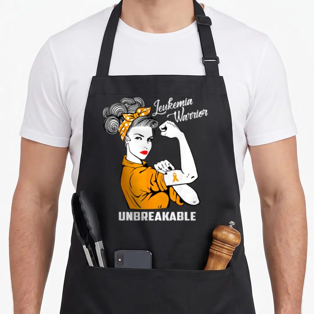 Leukemia fighter apron - Woman flexing arm with orange ribbon tattoo and Leukemia Warrior Unbreakable text — shown on a black cotton canvas apron against a white background