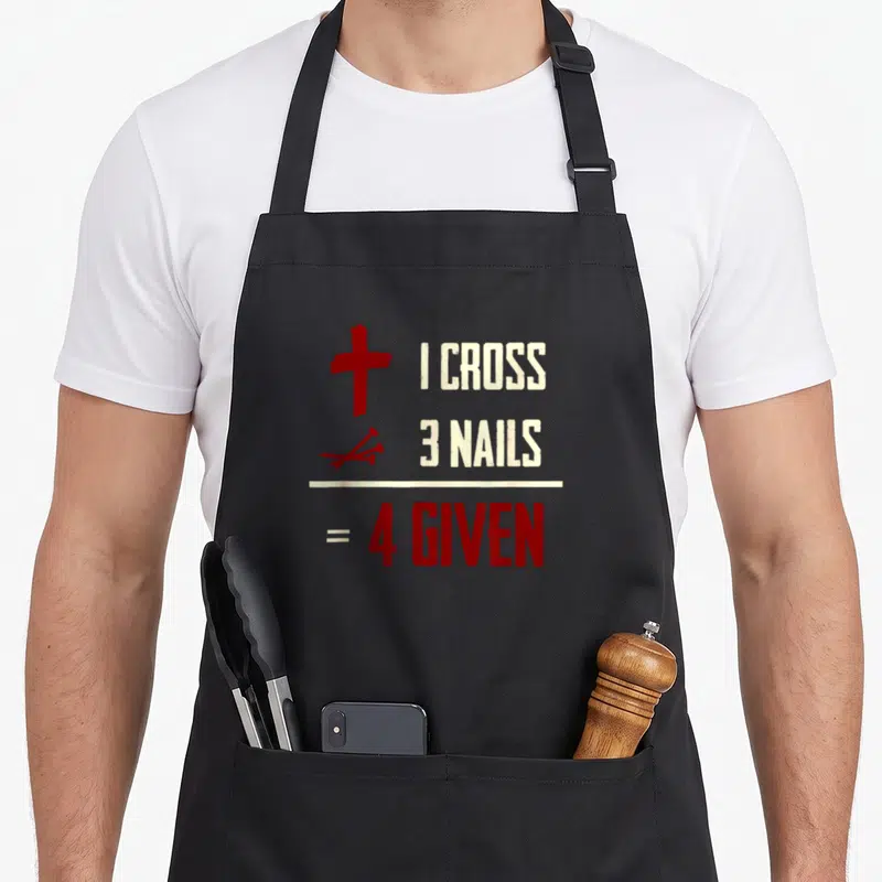 Correspond cross apron - Red cross and three nails beside beige text forming equation 4 Given — shown on a black cotton canvas apron against a white background