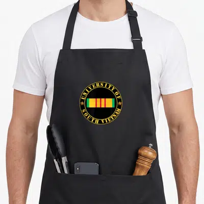 University vet apron - Circular seal with University of South Vietnam text and colored ribbon bar on black background — shown on a black cotton canvas apron against a white background