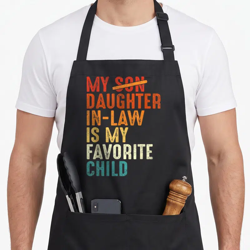 Daughter law father day apron - Stacked colorful text reading My Daughter in Law Is My Favorite Child with Son crossed — shown on a black cotton canvas apron against a white background