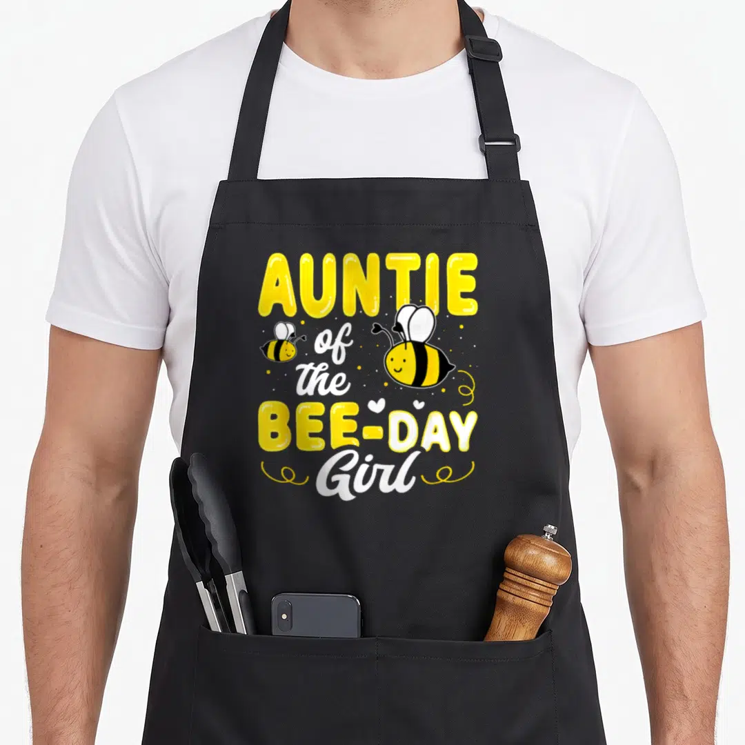 Auntie bee aprons - AUNTIE of the BEE-DAY Girl text with two cartoon bees, hearts, and dots — shown on a black cotton canvas apron against a white background