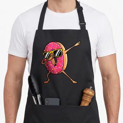 Hip donut apron - Dabbing donut character with pink frosting, yellow sunglasses, and tan limbs in cartoon style — shown on a black cotton canvas apron against a white background