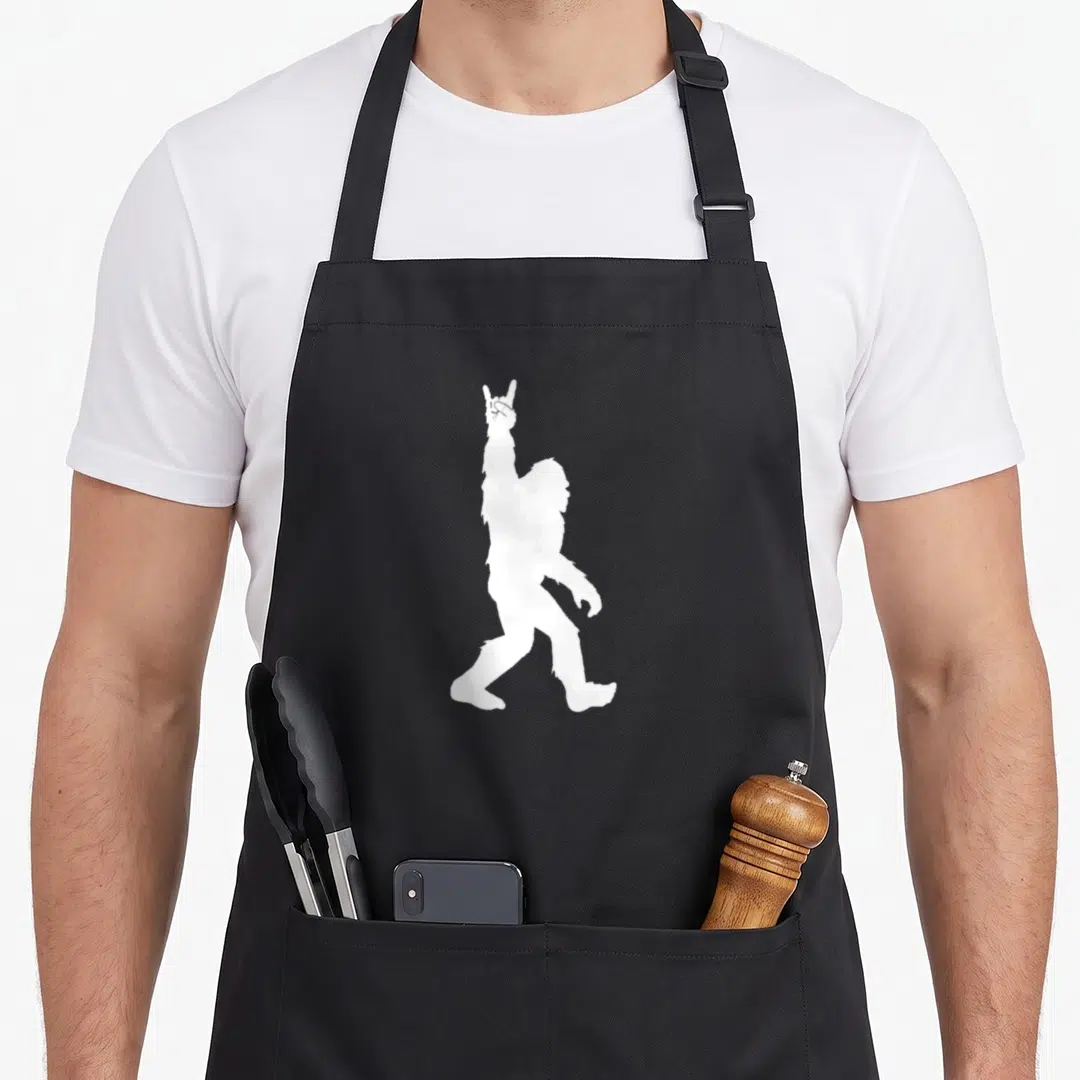 Roll sasquatch bigfoot apron - White Bigfoot silhouette walking and making a rock-on hand gesture — shown on a black cotton canvas apron against a white background