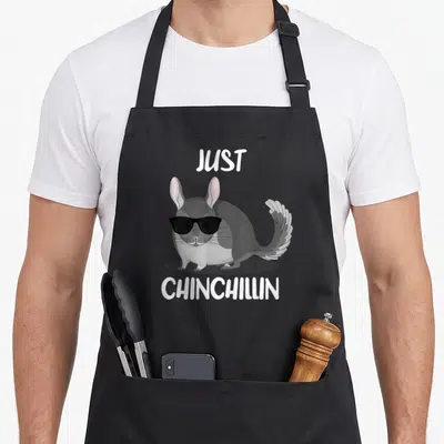 Chinchilla polka dot apron - Cartoon chinchilla wearing black sunglasses with text JUST CHINCHILLIN above and below — shown on a black cotton canvas apron against a white background