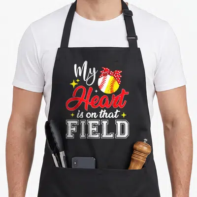 Field mother's day aprons - Softball with red polka dot bow and text My Heart is on that FIELD — shown on a black cotton canvas apron against a white background