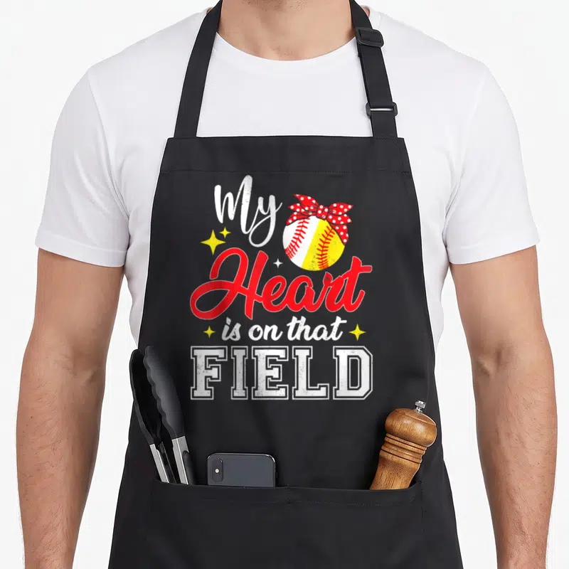 Field mother's day aprons - Softball with red polka dot bow and text My Heart is on that FIELD — shown on a black cotton canvas apron against a white background