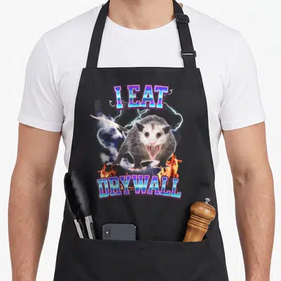 Eat raccoon eating apron - Opossum graphic with lightning and I EAT DRYWALL text — shown on a black cotton canvas apron against a white background