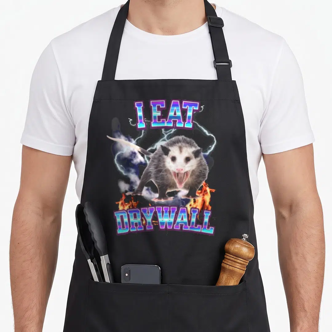 Eat raccoon eating apron - Opossum graphic with lightning and I EAT DRYWALL text — shown on a black cotton canvas apron against a white background
