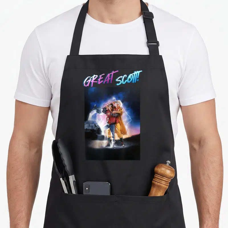 Scott future oil apron - Great Scott text arching over photo of two men standing by car with lightning — shown on a black cotton canvas apron against a white background