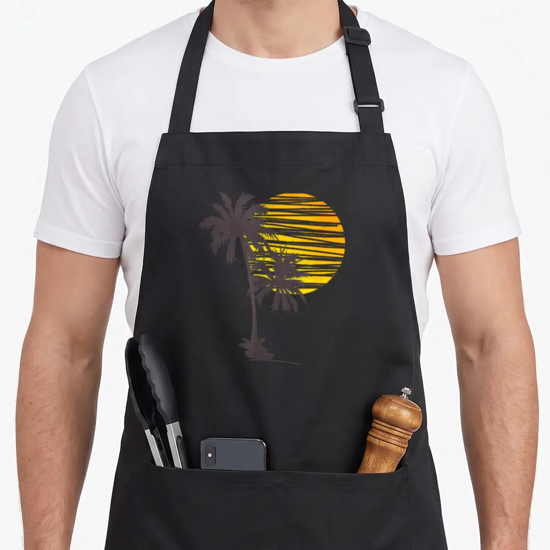 Beach holiday apron - Two dark grey palm tree silhouettes against a striped yellow-orange sun — shown on a black cotton canvas apron against a white background