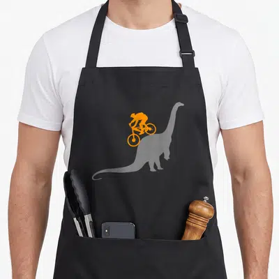 Mtb bicycle apron - Orange silhouette of a cyclist riding a bike on grey background — shown on a black cotton canvas apron against a white background