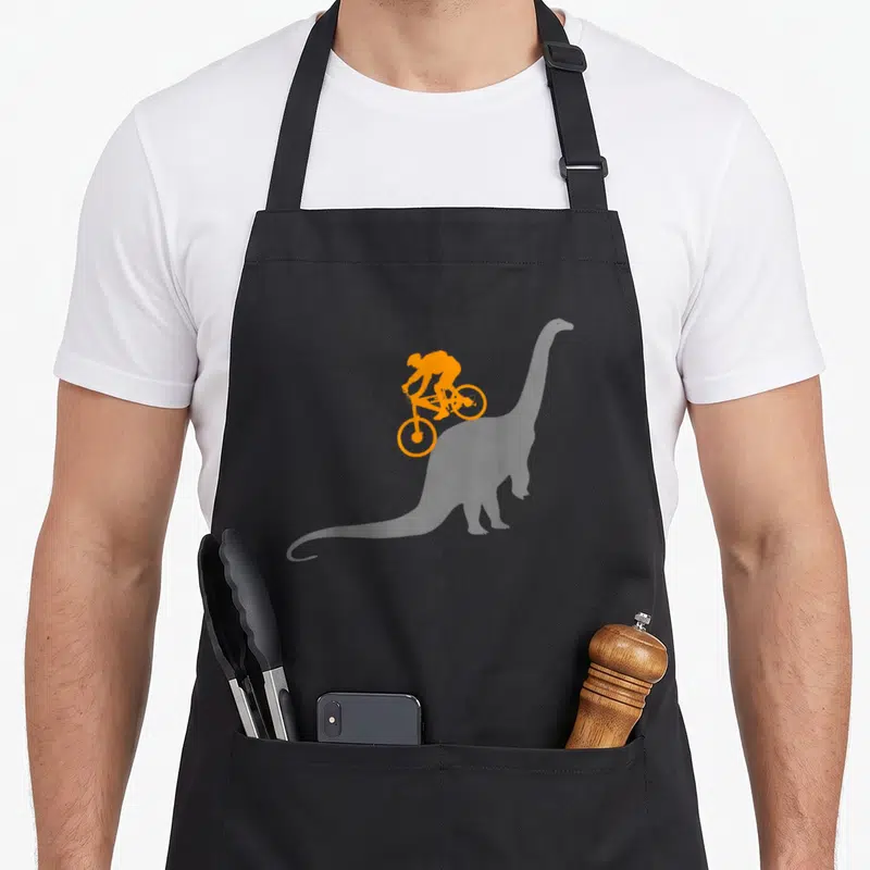 Mtb bicycle apron - Orange silhouette of a cyclist riding a bike on grey background — shown on a black cotton canvas apron against a white background