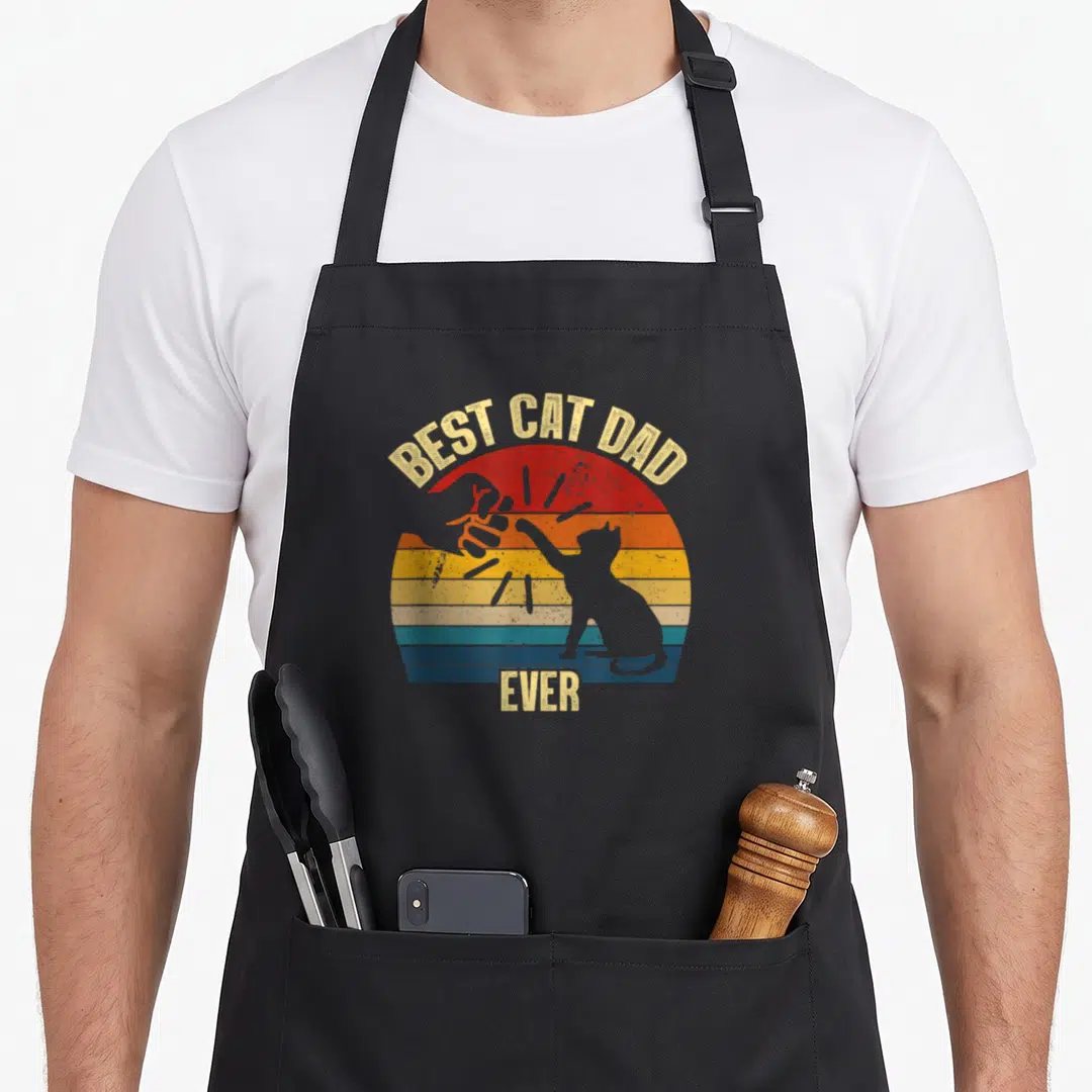 Funny daddy cat dad apron - BEST CAT DAD EVER text over striped sun with cat and thumbs up silhouette — shown on a black cotton canvas apron against a white background