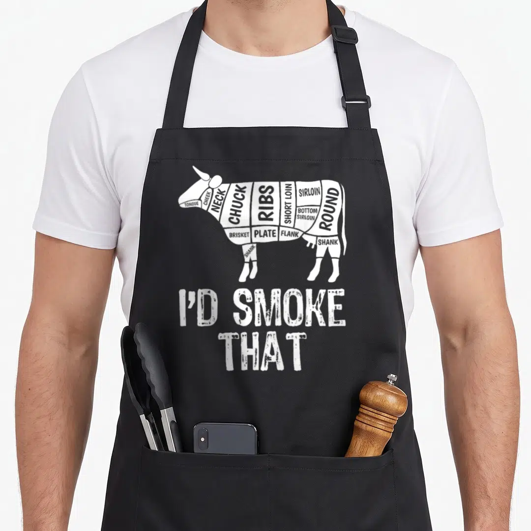 Cow barbecue apron - White cow diagram labeled with meat cuts and I'D SMOKE THAT text — shown on a black cotton canvas apron against a white background
