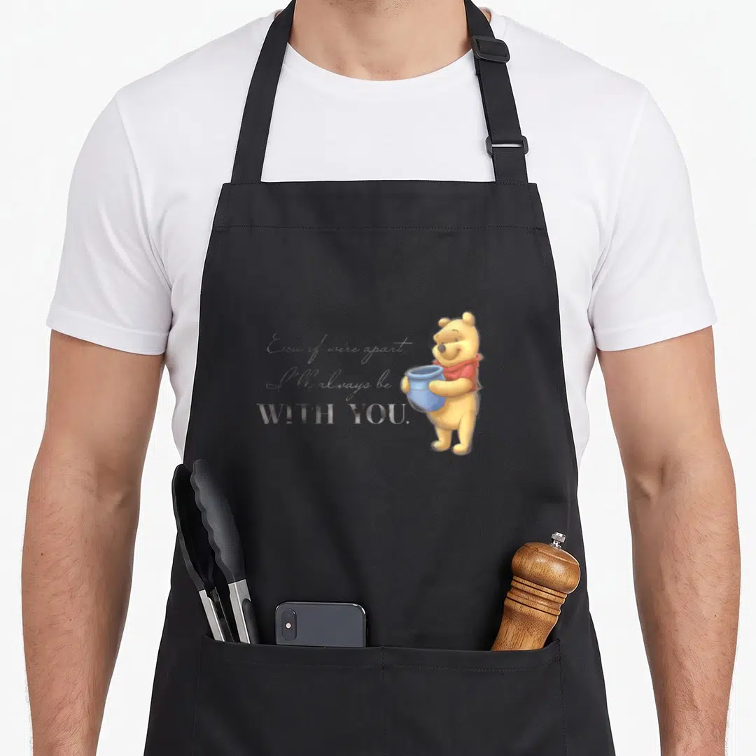 Anniversary novelty apron - Winnie the Pooh holding blue pot beside stacked quote text in yellow and red — shown on a black cotton canvas apron against a white background
