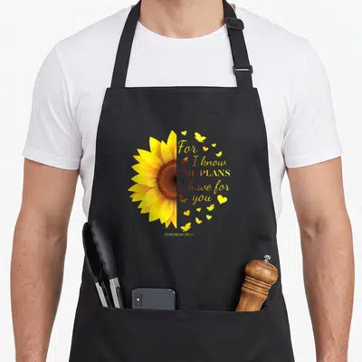 Jeremiah christian by alexis mae apron - Yellow sunflower half and Jeremiah 29:11 verse with butterflies and hearts — shown on a black cotton canvas apron against a white background