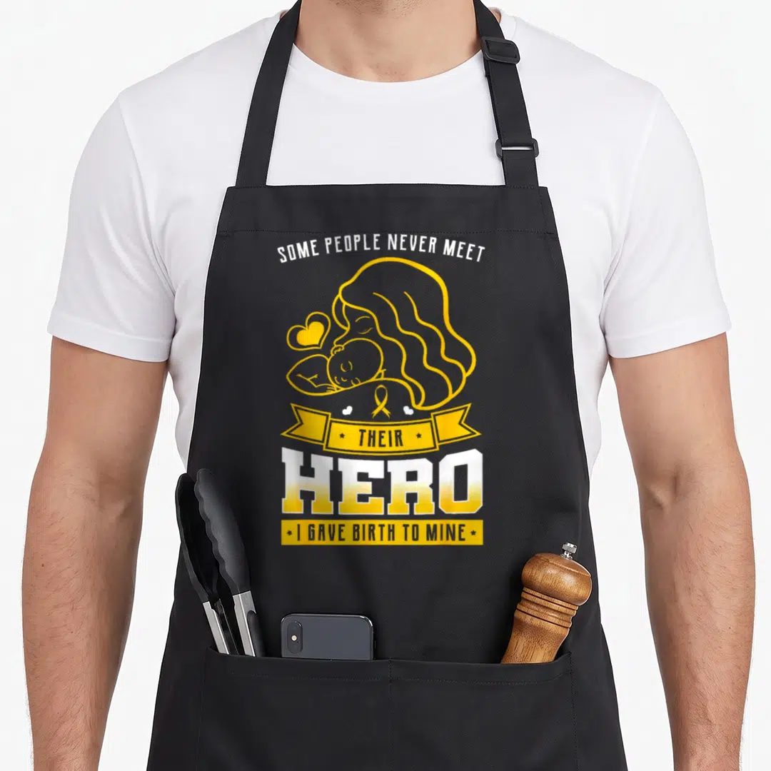 Meet pediatrician mom apron - Mother and baby line art with yellow ribbon and text about giving birth to a hero — shown on a black cotton canvas apron against a white background