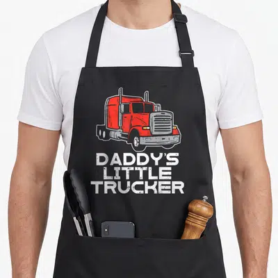 Trucker trucking semi truck apron - Red cartoon semi truck above white Daddy's Little Trucker text on grey background — shown on a black cotton canvas apron against a white background