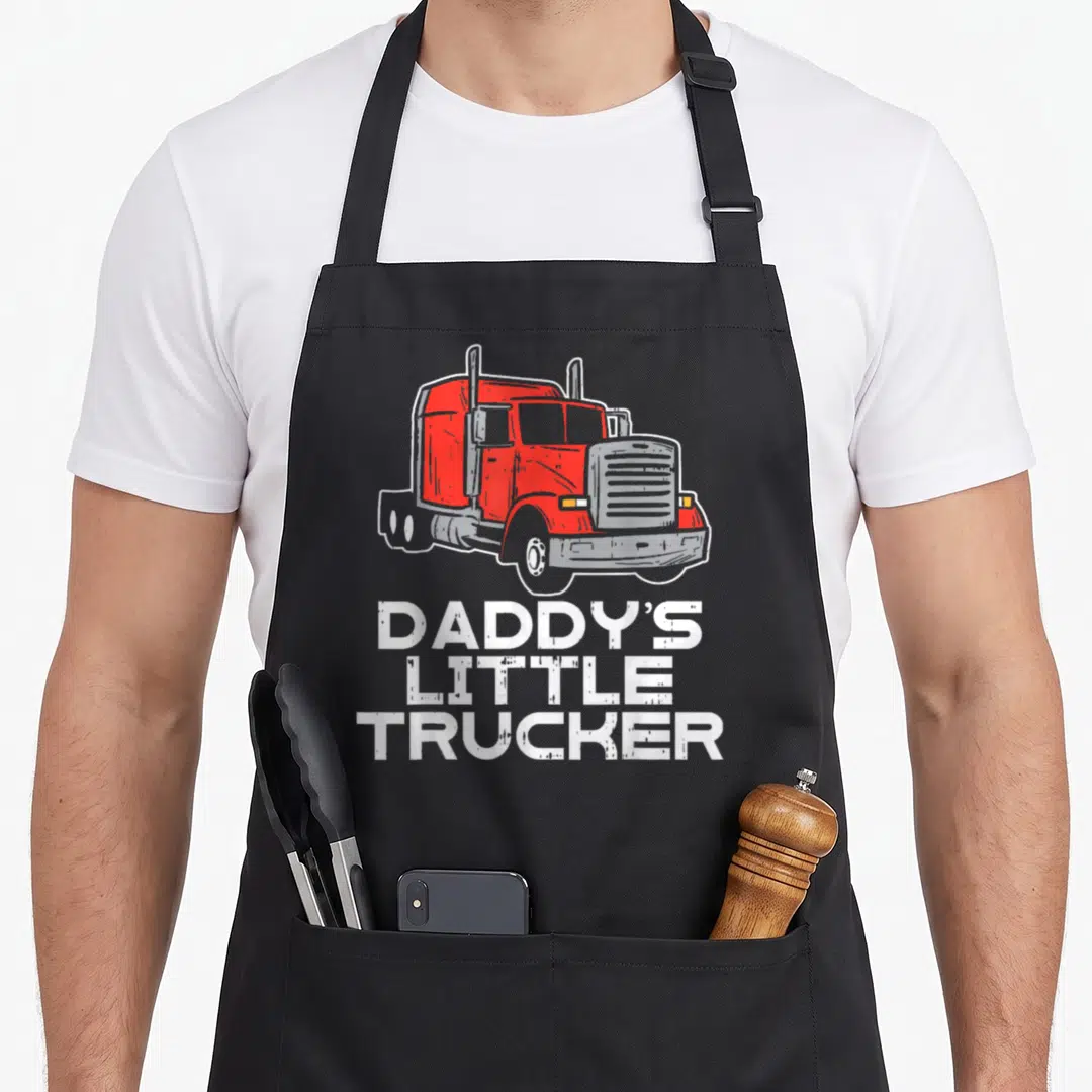 Trucker trucking semi truck apron - Red cartoon semi truck above white Daddy's Little Trucker text on grey background — shown on a black cotton canvas apron against a white background
