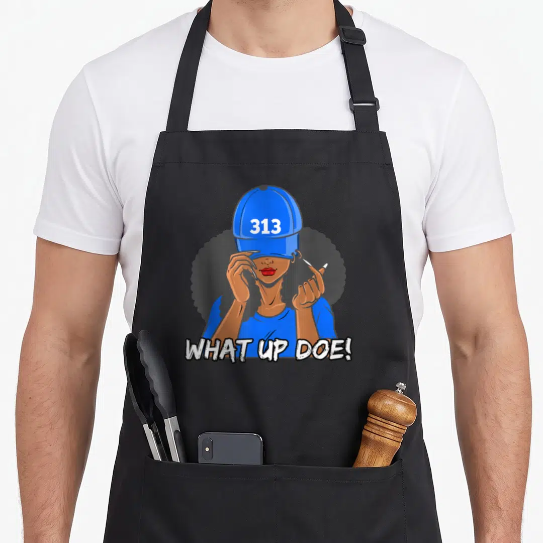 Afro detroit apron - Cartoon woman in blue cap with 313 and What Up Doe text — shown on a black cotton canvas apron against a white background