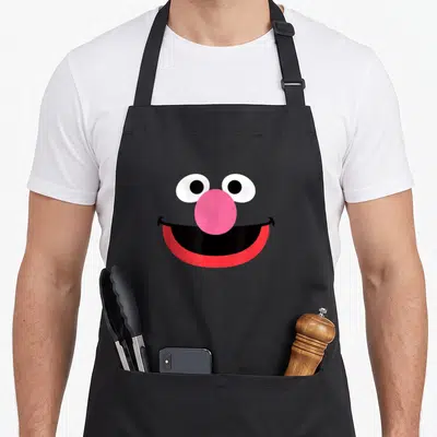 Grover halloween apron - Cartoon face with pink nose, red mouth, white eyes, and black outlines — shown on a black cotton canvas apron against a white background