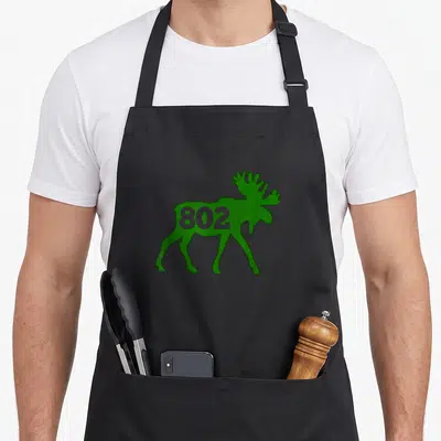 Moose vermont apron - Green moose silhouette with 802 and Vermont state map printed inside — shown on a black cotton canvas apron against a white background