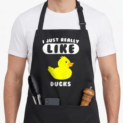 Duck apron for women - Cartoon yellow rubber duck with I Just Really Like Ducks text in white and grey — shown on a black cotton canvas apron against a white background
