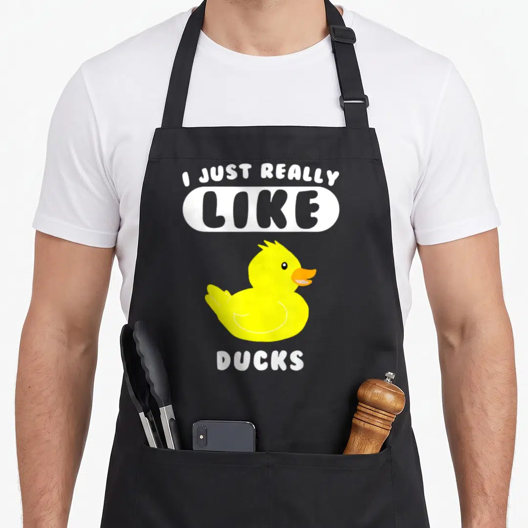 Duck apron for women - Cartoon yellow rubber duck with I Just Really Like Ducks text in white and grey — shown on a black cotton canvas apron against a white background