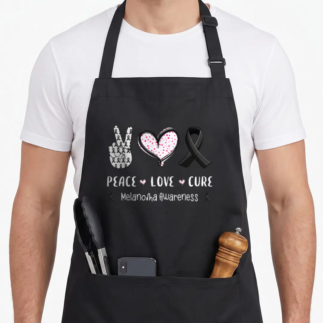 Peace melanoma awareness apron - Peace sign with ribbons, pink heart, black ribbon, and PEACE LOVE CURE text — shown on a black cotton canvas apron against a white background